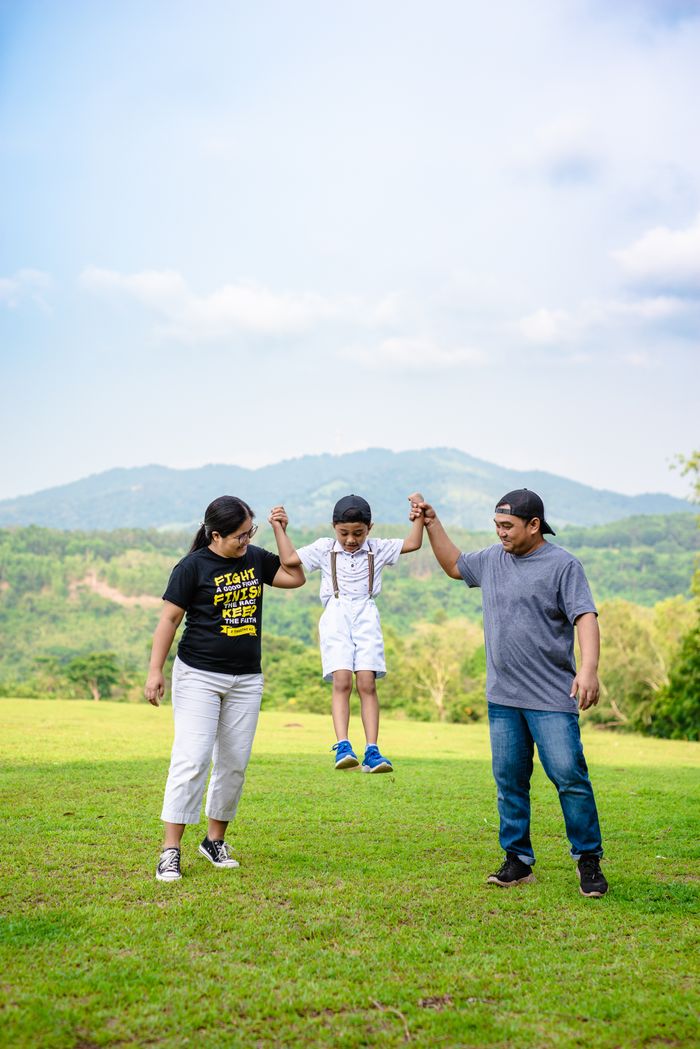 Offering A joyful family moment with parents lifting their child in a green field.